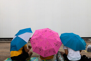 Group of people with rain umbrella waiting queue for watching outdoor movie, Bangkok Thailand.Group of people with rain umbrella sitting and waiting on the floor in Rainny day.
