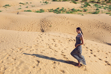 brunette woman in a long leopard dress walk with her back in the desert at sunset. go everywhere.