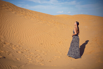 brunette woman in a long leopard dress stands with her back in the desert at sunset. go everywhere.