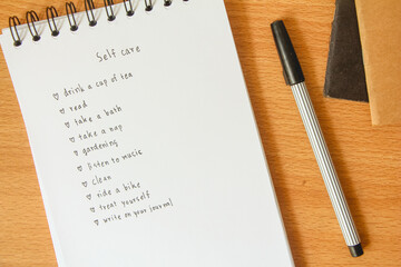 Text list for self care on notebook with pen on white background, office desk.