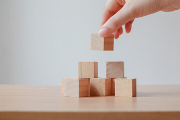 Hand putting wood cube on top of wood block stacking as step stair. business growth to success.