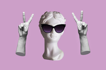 Antique female statue's head in black sunglasses showing a peace gesture with hands isolated on a...