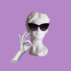 Confident antique female statue's head in black sunglasses shows the ok gesture with hand isolated...