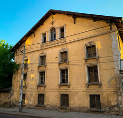 Fototapeta premium An abounded old beautiful house with crumbling facade. Vintage yellow town mansion with gorgeous exterior in bad condition.