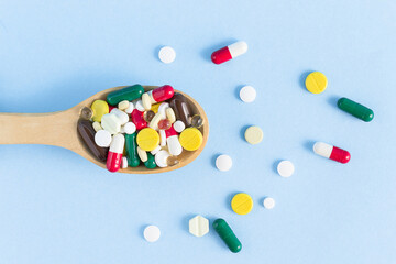 Top view of a wooden spoon filled with various pills on a blue background