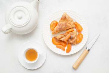 Homemade peach pie with teapot, cup of tea knife on white background. Top view.