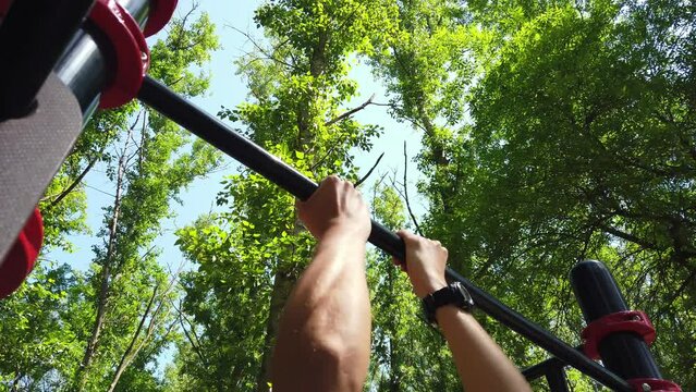 Low angle view of man pulling himself up on a crossbar at outdoor workout ground. Outdoor chin-ups exercising