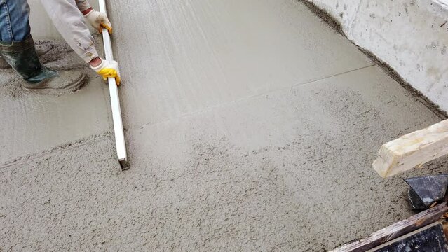 Construction worker uses trowel to flatten cement mortar screed. Concrete works on construction site. Cast-in-place work using trowels. 