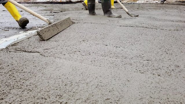 Construction worker uses bullfloat to flatten cement mortar screed. Concrete works on construction site. Cast-in-place work using trowels. 