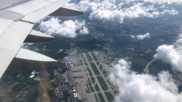 Cabin view of plane wing and airport runways and clouds