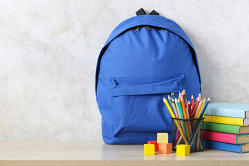 A blue school backpack, textbooks and pencils on the desk.