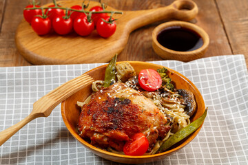 Udon with vegetables and chicken on the table in a wooden plate next to champignons and tomatoes on a plank and a wooden fork.