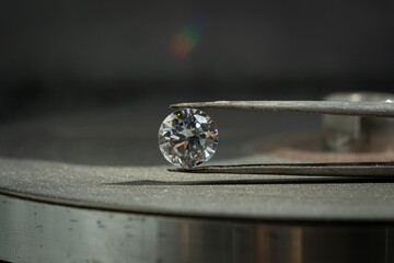 close up photo of round Diamond in Tweezers on polishing surface