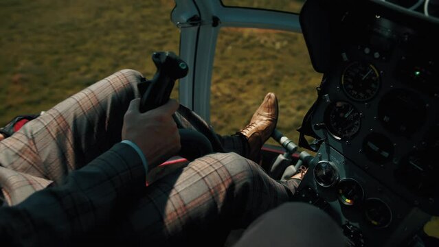 A pilot in a business suit controls a helicopter joystick flying over green fields