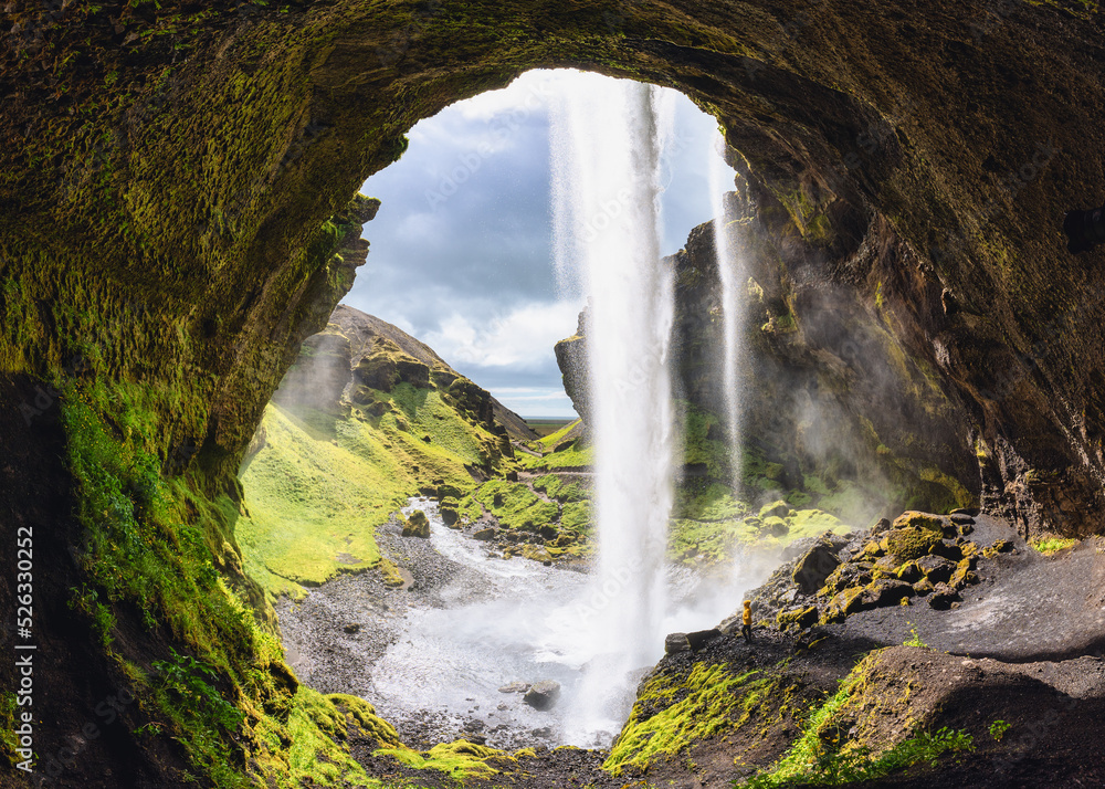 Wall mural Kernufoss waterfall flowing from cliff and hiker standing in summer at Iceland