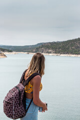 blonde woman in bikini with a backpack looking at a lake