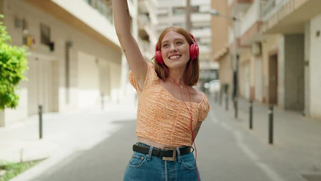 Young redhead woman listening to music dancing at street