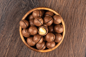 Macadamia nuts in shell and without in a wooden bowl.