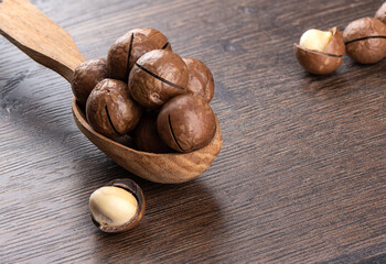 Macadamia nuts in a wooden spoon and a few on a wooden background.