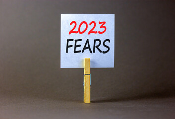 2023 Fears symbol. White paper with words 2023 Fears, clip on wooden clothespin. Beautiful grey table grey background. Business and 2023 fears concept. Copy space.