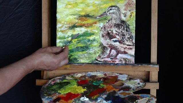 A man's hand paints a duck with a palette knife. The process of creating an oil painting with a palette knife