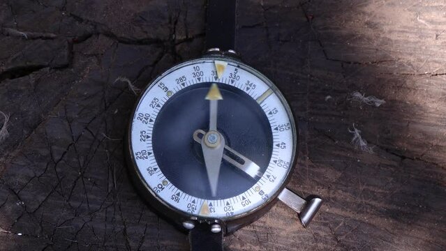 The compass needle is moving. Male hands trigger the arrow of a vintage compass lying on wood