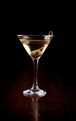 close-up on martini cocktail glass with olive. james bond 007 vesper and wooden table