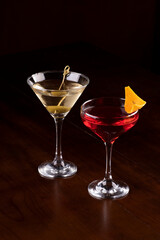 two cocktail glasses with martini, olive and orange on rubber stand on pub counter viewed from an angle