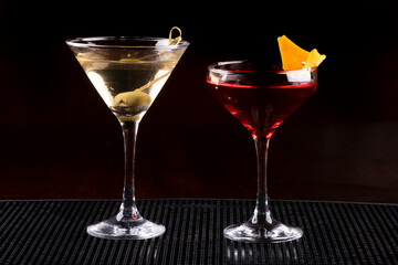 two cocktail glasses with martini, olive and orange on rubber stand on pub counter