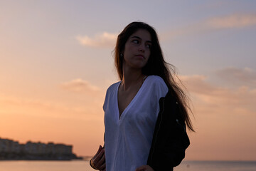 young hispanic girl posing at the rocks of a beach in the mediterranean sea while sunrise