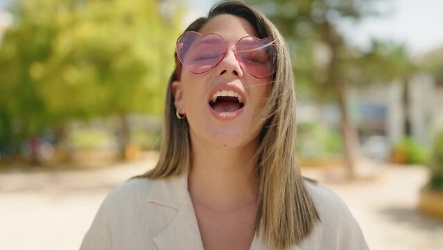 Young hispanic woman smiling confident wearing heart sunglasses at park