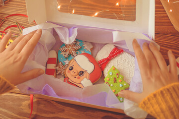 Women's hands open gift box with Christmas cookies. Gingerbread cakes with colorful icing. Festive sweets for children in form of pig, mittens, pine tree and snowflakes. New Year's composition.