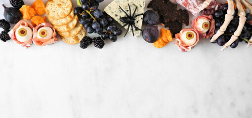 Halloween theme charcuterie top border against a white marble background. Collection of cheeses and meat appetizers. Copy space.
