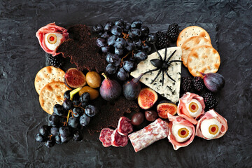 Halloween theme charcuterie board. Above view against a dark background. Assortment of cheese and...
