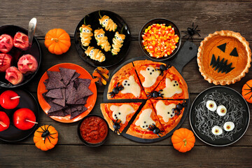 Fun Halloween dinner party table scene over a dark wood background. Top view. Pizza, jack o lantern...