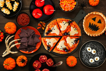 Fun Halloween dinner party table scene over a dark wood background. Overhead view. Pizza, jack o...