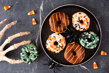 Variety of spooky Halloween themed donuts. Top down view table scene on a dark stone background with skeleton hand.