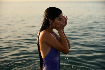 young girl wearing a purple swimming suite taking a morning bath on the mediterranean sea at the sunrise in a warm summer day