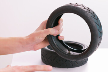 A male hand holds a small scooter tire with inner tube with valve on a white background. Wheel....