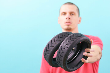 A man holds two small scooter tires in front of him on a blue background. Wheel. Rubber. Black....