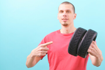 A man holds two small scooter tires and pointing his finger on it on a blue background. Wheel....