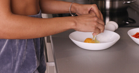 Woman cracking eggs into glass bowl.