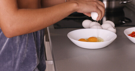 Woman cracking eggs into glass bowl.