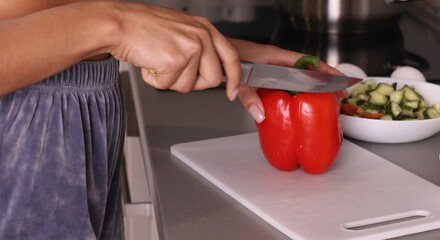 Girl cook in the kitchen cuts red paprika with vegetables with a knife.