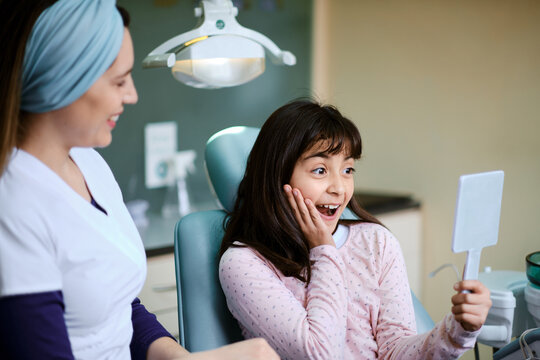 Girl looking into a mirror with a surprised expression in the dentist's chair