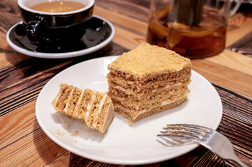 Still life with dessert: honey cake in a white plate and a cup of tea in a cafe