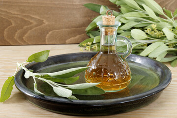 Herbs infused vinegar in bottle. Sage leaves with natural oils bottle. Herbalism concept. - obrazy, fototapety, plakaty