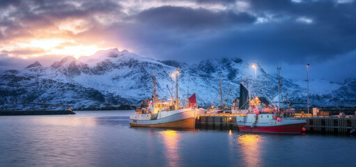 Fishing boats on the sea, snowy mountains, colorful sky with clouds at sunrise in Lofoten islands,...