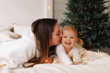 Obraz na płótnie Canvas Portrait of an emotional happy candid mother and child little girl having fun and hugging on Christmas day in a cozy decorated room at home in December. Selective focus