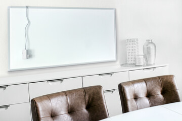 Weisse elektrische Infrarotheizung im Wohnraum mit Netzkabel und Thermostat